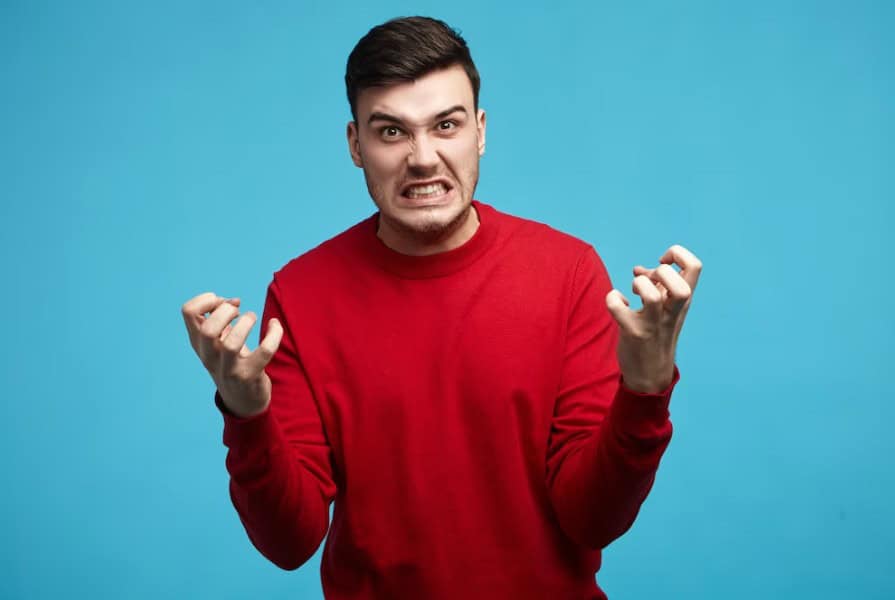 Angry adult man with an expressive face in a red jumper against a blue background.