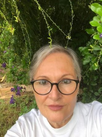 Cath Covacin Portrait of a Cath Covacin with glasses, posing in a lush garden.