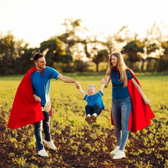 Family mental wellbeing Family with red capes swinging a child between them in a field